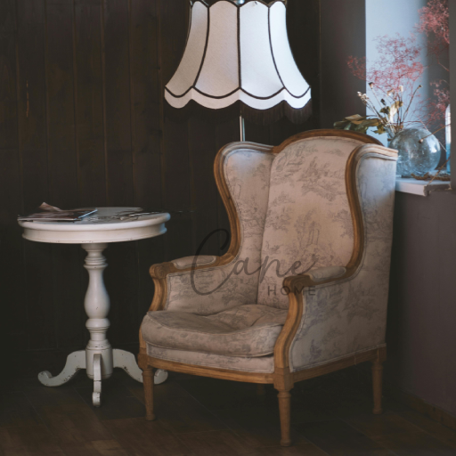 كرسي برجير فرنسي كلاسيكي منقوش برسومات ريفية مع طاولة جانبية بيضاء وأباجورة قماشية في ركن قراءة هادئ.